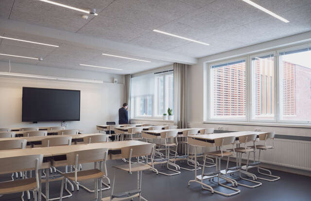 An interior photo of a classroom with a row of windows along the external wall and numerous desks and chairs.