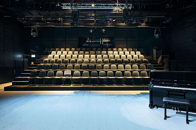 View from scene with a piano towards an auditorium with beige chairs