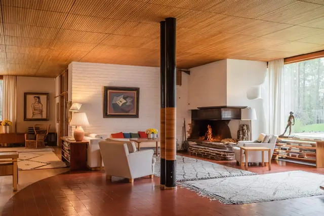 A space with wooden ceiling and red tiled floor, white foreplace in the corner next to a glazed wall