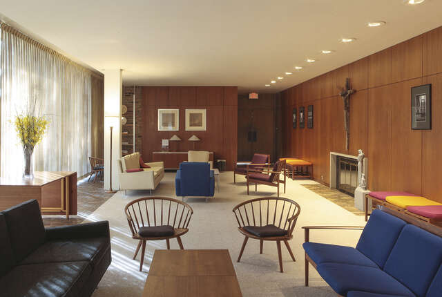 A room with a floor-to-ceiling window on the left, wood-panelled walls and couches and armchairs