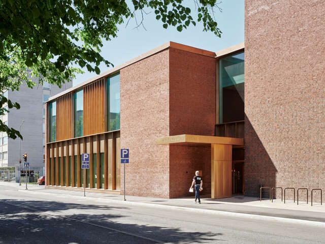 A red-brick building fronting the street, with tall, vertically proportioned windows framed in bronze.