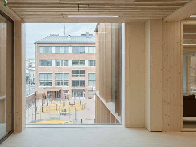 A timber-clad interior space with a large window overlooking a playground.