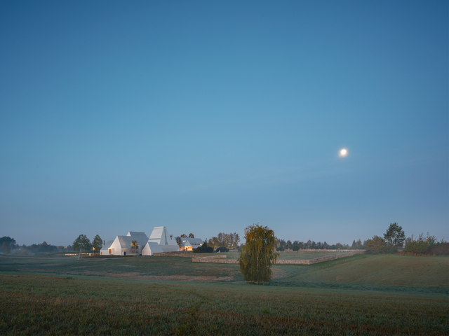 A hazy photo of a green field, with a silver building in the background featuring gabled roofs of varying heights.