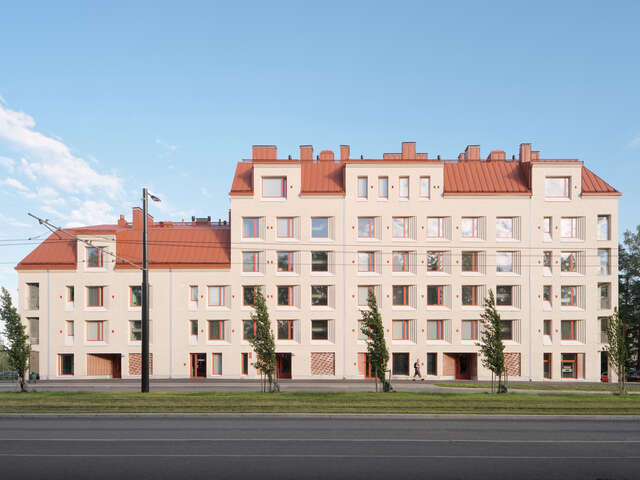 Brick apartment building with square window recesses and red roof.