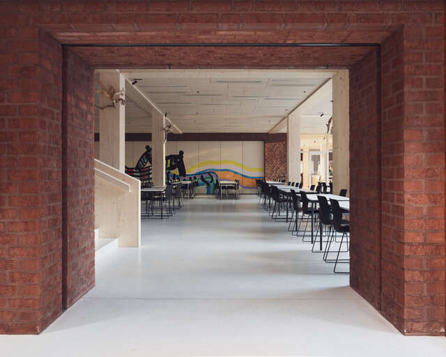 An interior photograph showing a red-brick opening onto an open canteen space supported by timber columns.