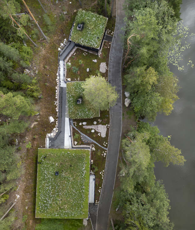 Aerial view of three buildings with green roofs, connected by a wooden pathway.