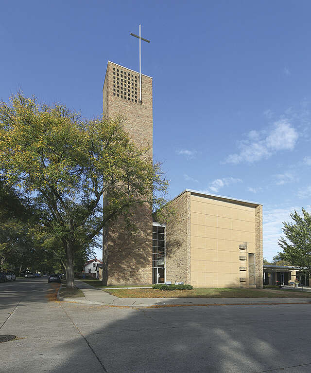 A box-like building and a high tower with a cross, primary material yellow brick