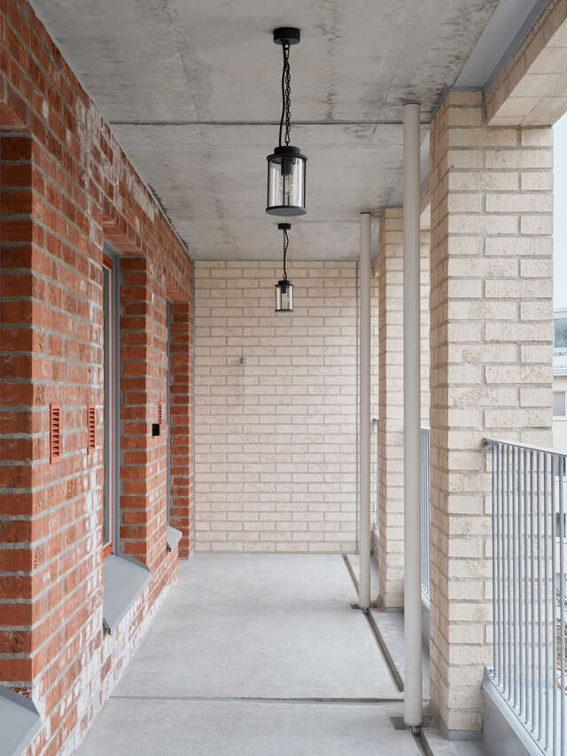 An empty balcony. Red brick wall on the left and light brick columns on the right.