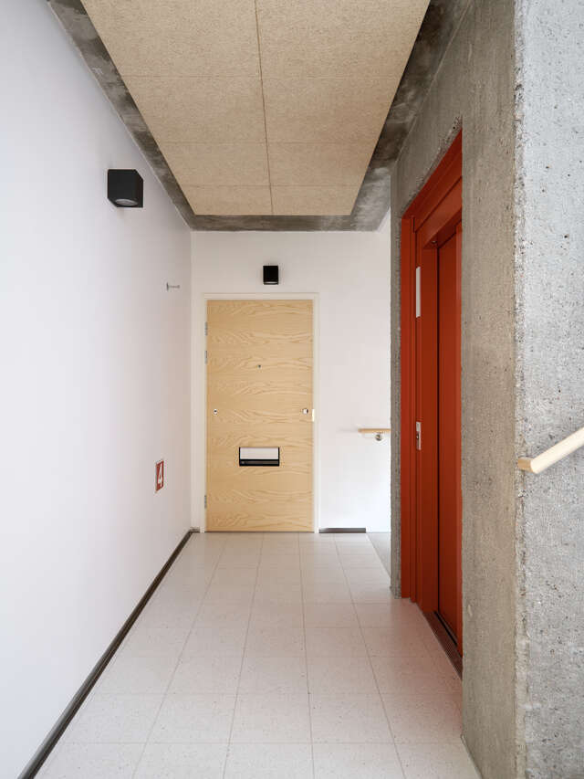 Red lift door on the right and wooden apartment door down the hall.