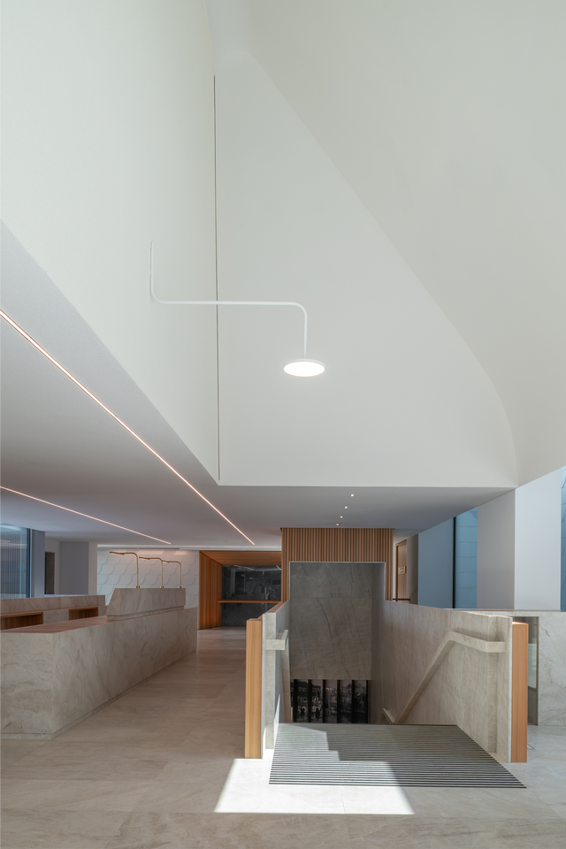 An interior photo featuring marble surfaces, varying ceiling heights, and a staircase leading to the lower level.