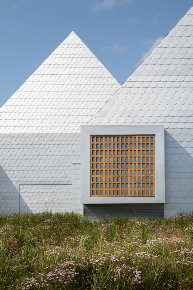 Two aluminium-clad buildings with pitched roofs, one featuring a square projecting element with a timber slatted facade.
