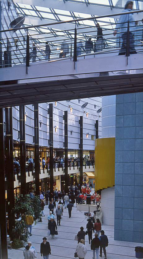 People walking in a curved gallery with a glass roof.
