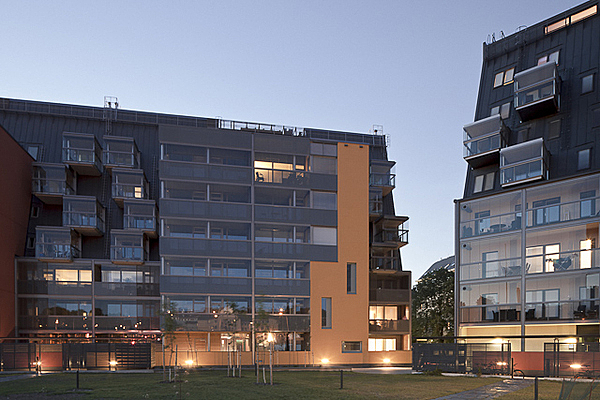 Back facade of the apartment building with large glass balconies, a black roof and burnt orang colored plaster.