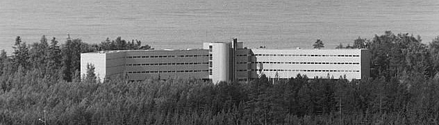 Birds eye view of the white hotel building surrounded by trees and with the sea in the background.