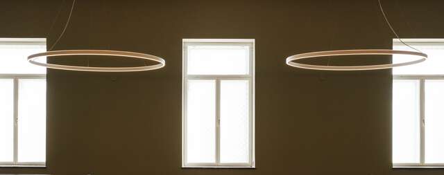 Beige wall with three windows and two circular hanging lamps.