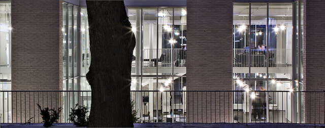 Courtyard facade during the evening with lights on inside the building, students are visible in the building.