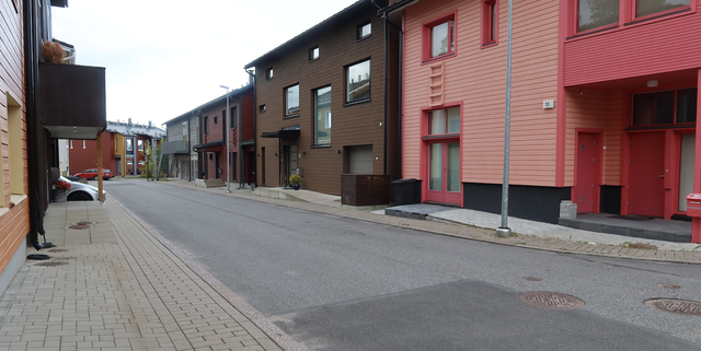Colourful wooden houses in a row with asphalt street in foreground.