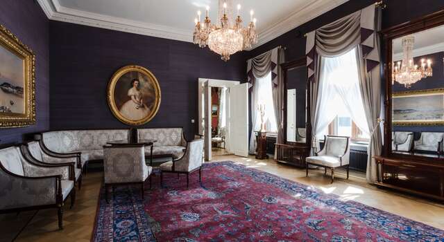 Sitting room with gold framed portraits, a seating arrangement with silver thread embroidery and a Persian rug.