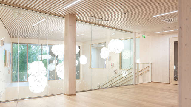 Wooden floor and ceiling, glass wall with a view towards a space with hanging lamps