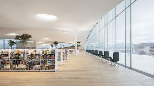 Comfortable interior of the library with bookshelves and seating arrangements. At the right there is a glass wall with doors to the terrace.