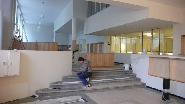 A man sitting on stairs and working on the restauration, the surroundings are not ready yet and there repaint buckets and work tools laying around.