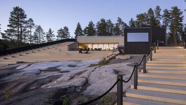 Waterfront with rocks in foreground and large wooden structure with staircase in background.