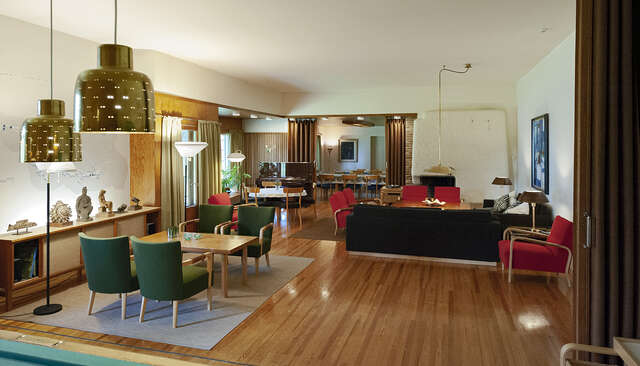 The sophisticated interior architecture with various design furniture and artefacts as well as a beautiful, white plastered fireplace in the corner. Flooring is made of a beautiful shade of wood, as is are the wall panels around the windows. Otherwise the walls, as well as the roof, are white.