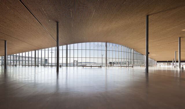 Spacious terminal interior with a wooden curved ceiling and a glazed outer all.