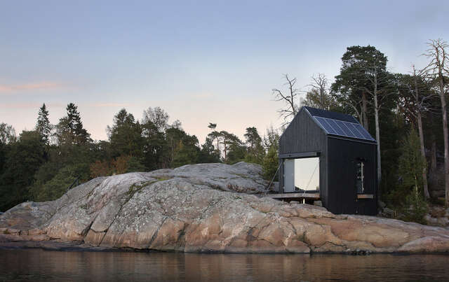 A small black cabin built on a rock.