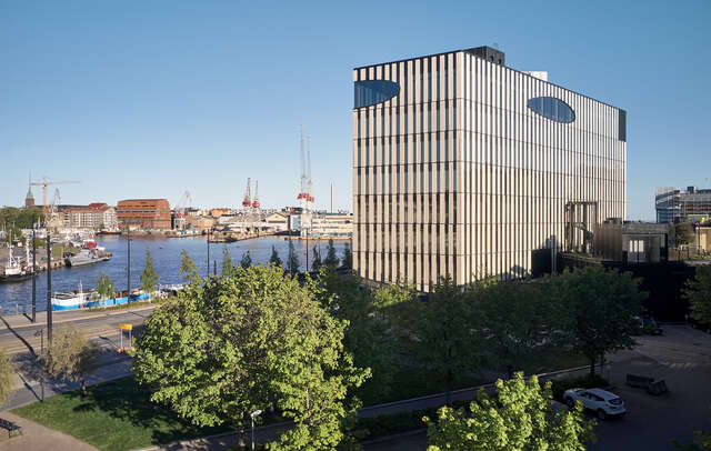 A large wooden building seen entirely, with a park in the foreground.