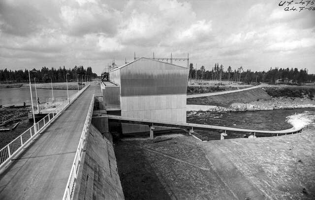 Image of abridge that spans over the river. Next to the bridge lies the power plant building.