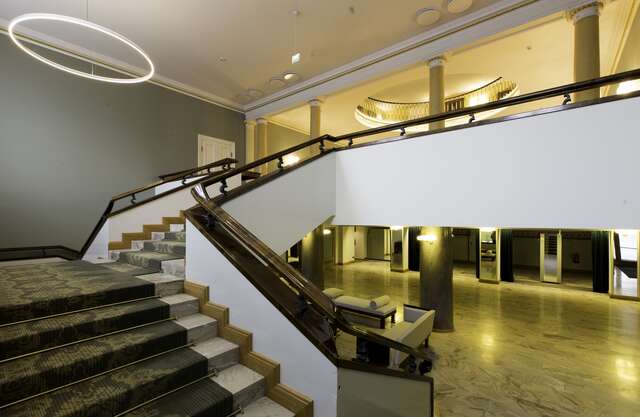 Staircase with marble stairs, a grey ornate rug, white and brown railings.