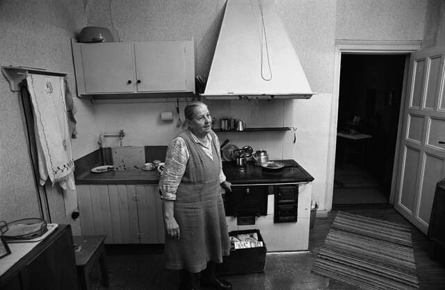 Black and white picture of an old woman in the kitchen.