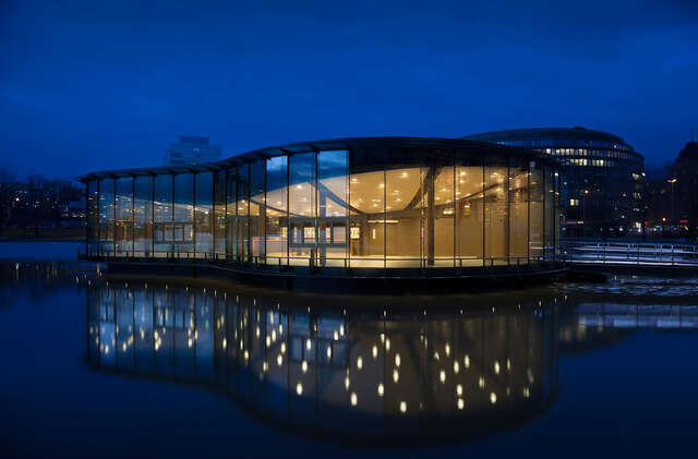 Curved glass facade of the restaurant viewed from the sea during the evening.