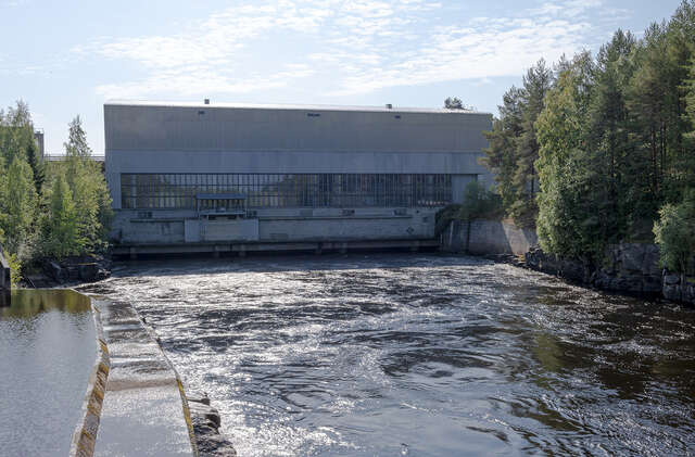 View over the river towards the hydropower plant with pitched roof and rectangular, vertical windows.