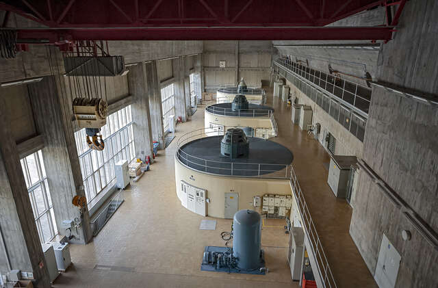 Interior view of the machine hall with round, yellow machinery and lots of natural light from rectangular windows.
