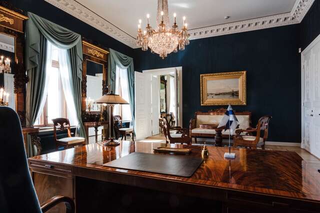 President's office with massive wood furniture, gold framed mirrors, a chandelier and dark blue walls.