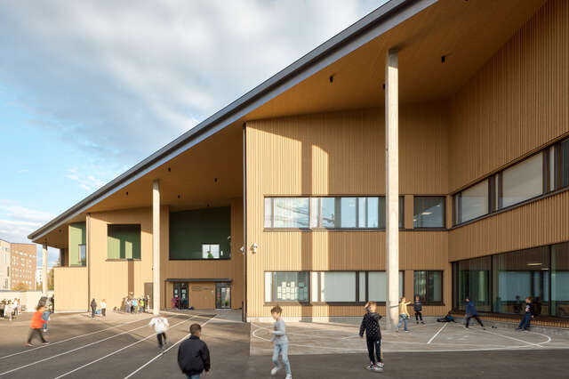 A large, multi story wooden building, with a yard full of small childfren.