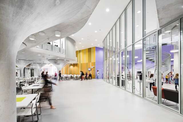 White and grey canteen with colure blue and orange wall on the background, a glass wall separates the space from the school library.