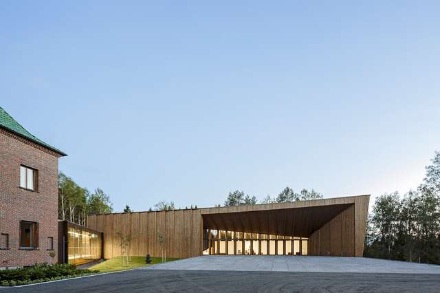wooden facade with a slanted roof, glass doors and a corridor connecting it to a red-brick building.
