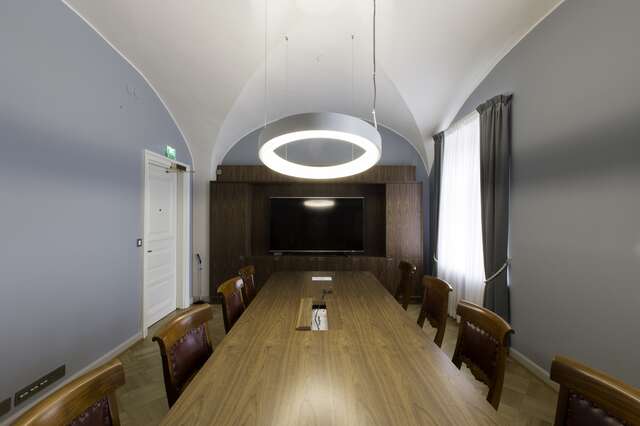 Meeting room with a long wooden table, blueish grey walls and a white groin ceiling.
