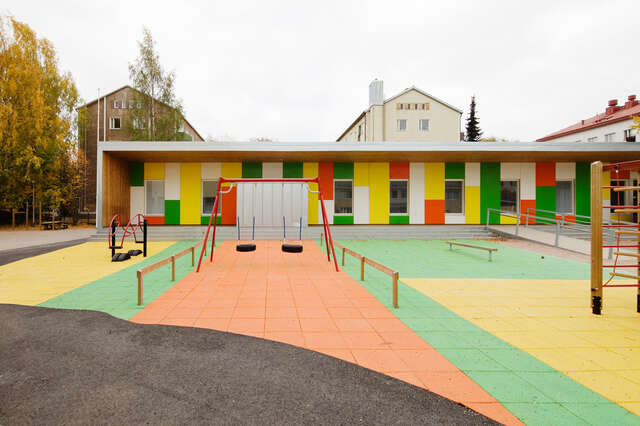 Yellow, green, white and red façade behind swings and colourful floor element