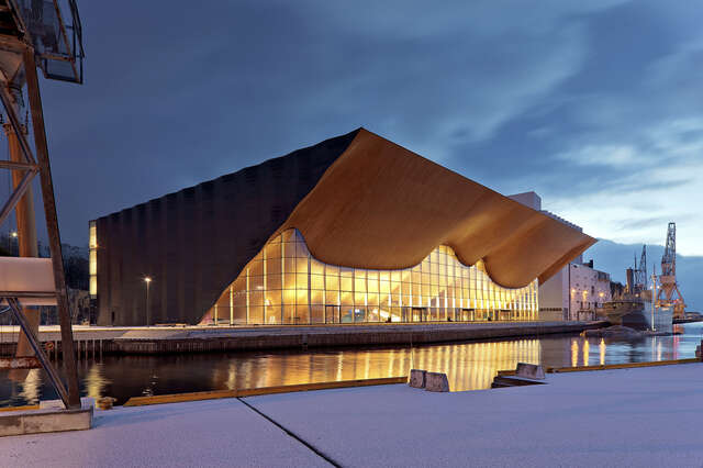 Evening view from across the harbour towards a building with a wavy wooden canopy