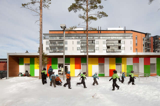 Children running in the snow in front of a colourful building