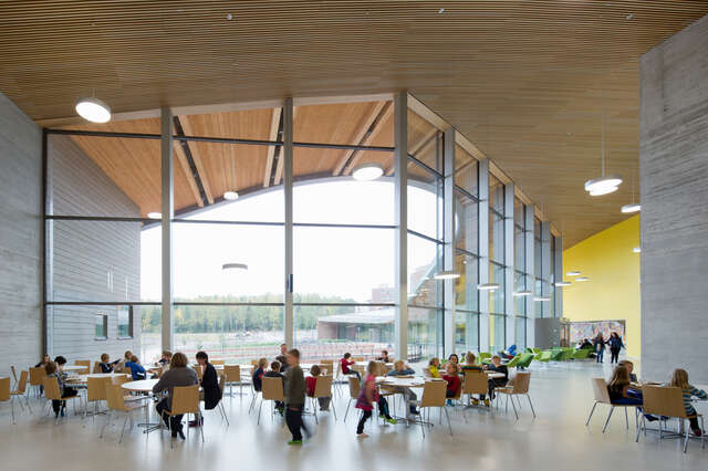 School children having lunch in a lobby next to a glass facade