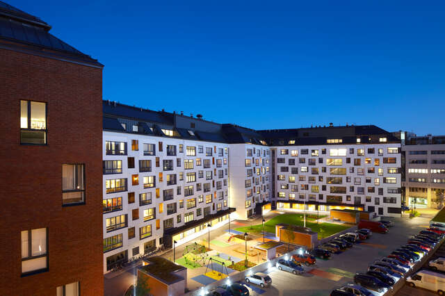 White housing block with square windows, playground and parking area in evening light