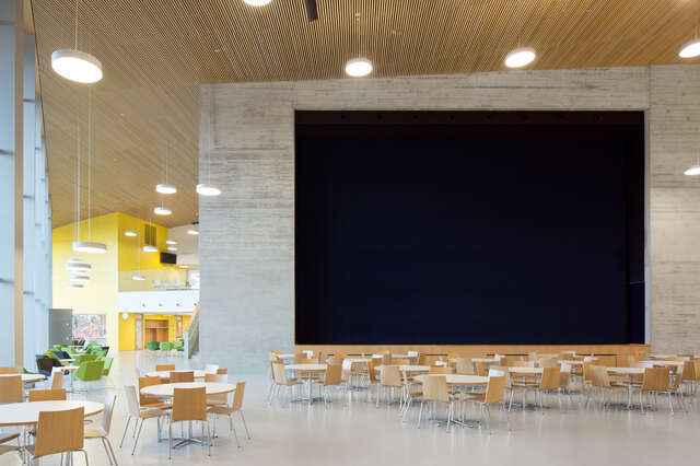 Chairs and tables in front of a large screen on a concrete wall, hanging white lamps, yellow back wall