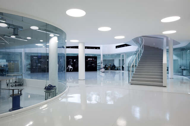Shining white floor, glass walled space on the left and stairs rising in on the right