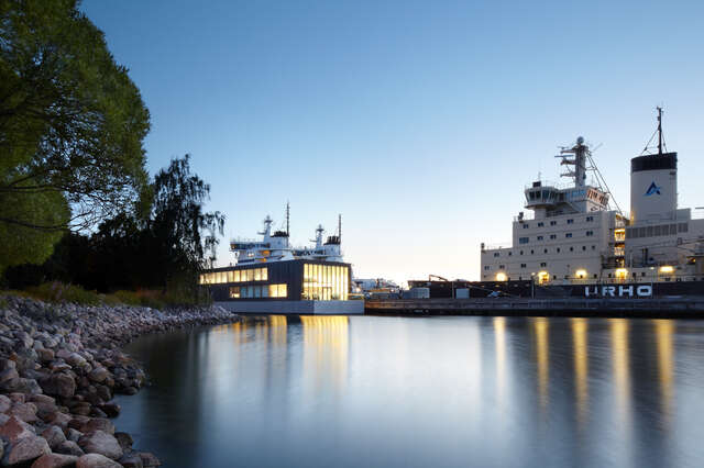 Illuminated horizontal building on the sea side with two icebreakers in the background