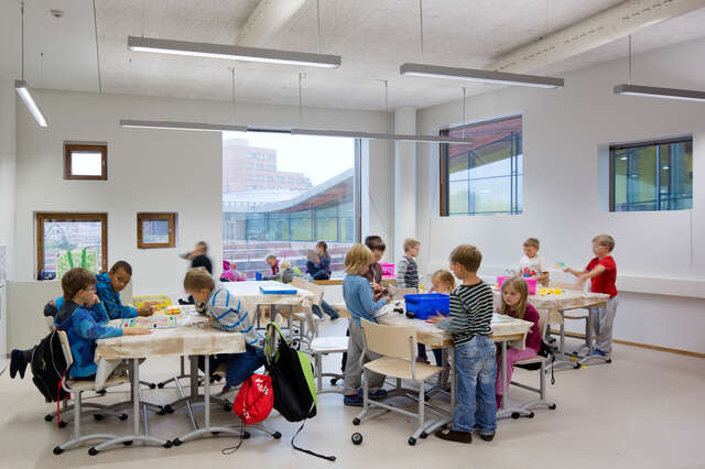 Children playing games in a white class room with windows to the school yard